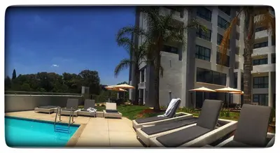 a pool with lounge chairs and umbrellas next to a building at Regency Menlyn Hotel 1Bed Apartment LongStay 32 percent off in Pretoria