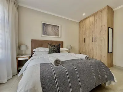 a bedroom with a large bed and a wooden cabinet at Midrand 2-Bedroom Oasis in Glen Austin in Midrand