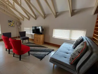 a living room with a couch and red chairs at Highlands Retreat Lodge In Highland Gate Golf and Trout Estate 1135 in Dullstroom