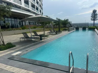 a swimming pool with chairs and an umbrella next to a building at Sunrise Waterfall at ELLIPSE in Midrand
