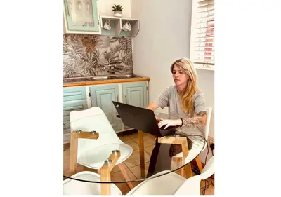 a woman sitting at a table with a laptop computer at Cottage of Grace in Benoni