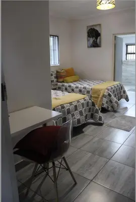 a room with two beds and a table and a chair at VinVid Harties Guest House in Hartbeespoort