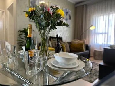 a glass table with a vase of flowers and a bottle of champagne at Indulge in Elegance & Comfort in Midrand