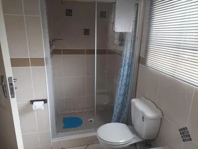 a bathroom with a toilet and a glass shower at Sleep Eezy Cottages in Benoni