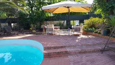 a patio with chairs and an umbrella next to a pool at Sleep Eezy Cottages in Benoni