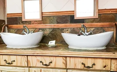 two sinks on top of a wooden cabinet with two mirrors at Corner View Accommodation in Kaapsehoop