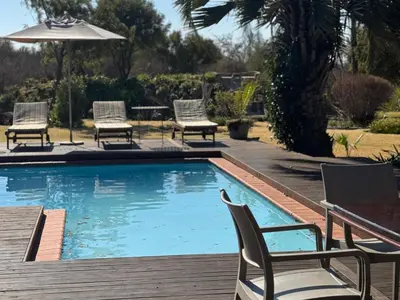 a swimming pool with chairs and an umbrella at Tshikwalo Guest House in Hammanskraal