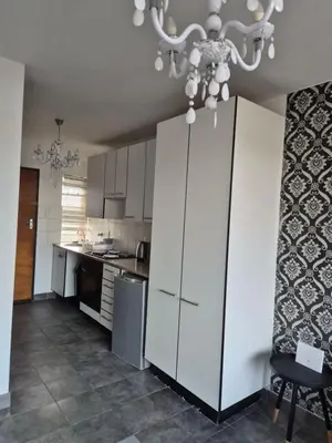 a kitchen with white cabinets and a chandelier at Elegant studio apartment in Hillcrest in Pretoria