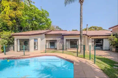 a house with a swimming pool and a palm tree at Guesthouse Charis in Pretoria