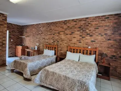 two beds in a room with a brick wall at Airport Inn Bed and Breakfast in Kempton Park