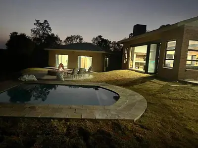 a woman sitting next to a swimming pool in front of a house at Elements Private Golf Reserve 123 in Warmbaths