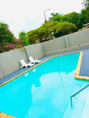 a swimming pool with two white chairs next to it at QHAWEKAZI GUEST HOUSe in Witbank