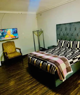 a bedroom with a bed and a chair and a tv at QHAWEKAZI GUEST HOUSe in Witbank