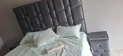 a bed with a black headboard with pillows and a table at Magoveni Accommodation