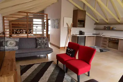 a living room with a red chair and a kitchen at Highlands Retreat Loft Unit in Highland Gate Golf and Trout 1135 in Dullstroom