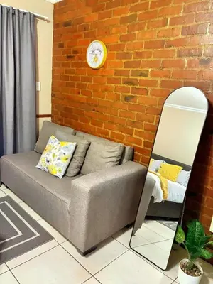 a couch against a brick wall with a clock at Apartment of Convenience-In the heart of Midrand in Midrand