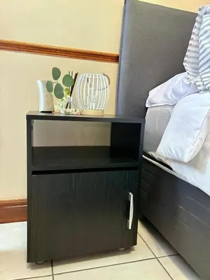 a black night stand next to a bed at Apartment of Convenience-In the heart of Midrand in Midrand