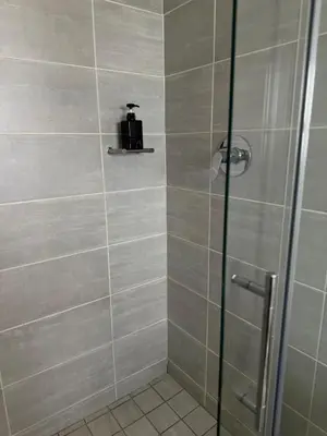 a shower with a glass door and a suitcase on a shelf at Zuri Marula Luxe in Midrand