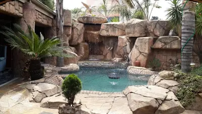 a swimming pool with a waterfall and a rock wall at Eagle Rock Executive Guest House in Kempton Park