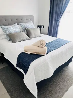 a white bed with a blanket and pillows on it at The Aura at Castle Gate in Pretoria