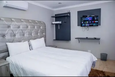 a bedroom with a white bed and a flat screen tv at Tindlovu GuestT House in Nelspruit