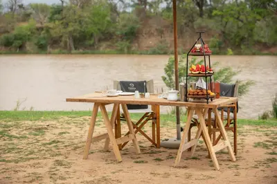 a wooden table with food on it next to a river at Kapama Southern Camp in Kapama Private Game Reserve