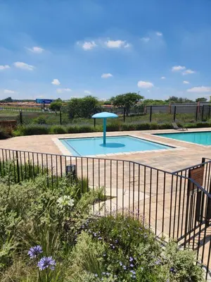 a swimming pool with a blue umbrella next to a fence at The white house in Midrand