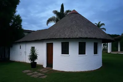 a small white building with a thatch roof at Nut Tree Nook in Hazyview