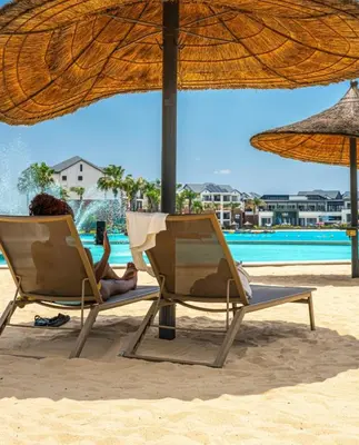 two people sitting in beach chairs under an umbrella on the beach at The Blyde Crystal Lagoon Pretoria in Pretoria