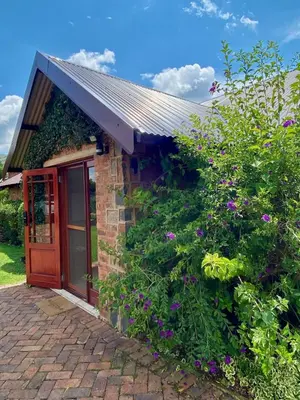 a brick house with a red door and flowers at Willow Weir River Cottage in Dullstroom
