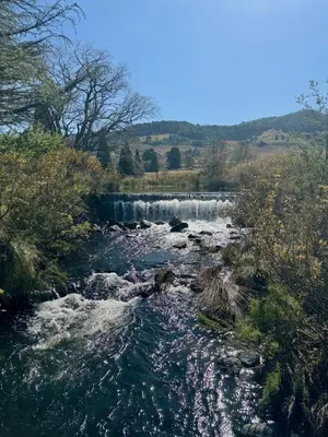a river with a waterfall in the background at Willow Weir River Cottage in Dullstroom