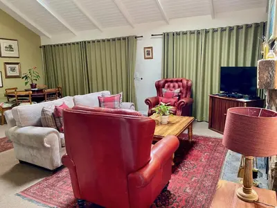 a living room with a couch and chairs and a tv at Willow Weir River Cottage in Dullstroom