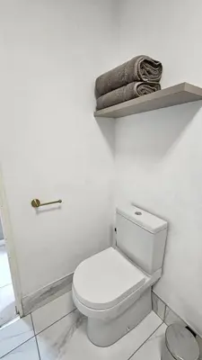 a white bathroom with a toilet and towels on a shelf at Critchley Hackle - Deluxe garden units in Dullstroom