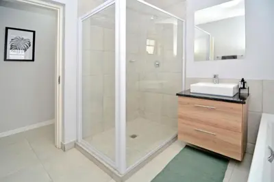 a bathroom with a shower with a sink and a mirror at Safubi 2 bedroom apartment in Nelspruit