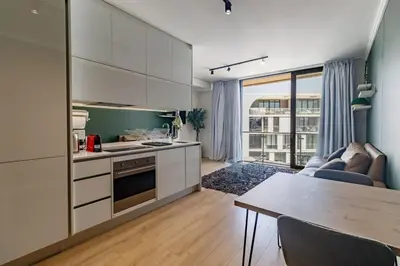 a kitchen with white cabinets and a living room at Ellipse Waterfall - Luxe Urban Escape in Midrand