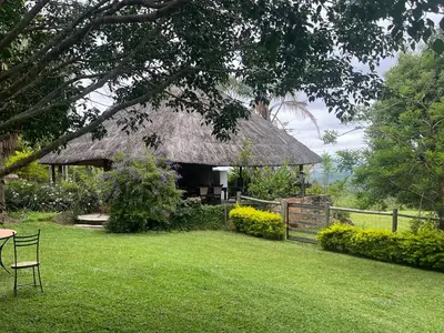 a building with a grass roof with a chair in a yard at Hooggelegen Estate in White River