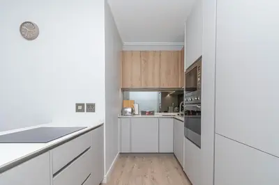 a white kitchen with white counters and wooden cabinets at Ellipse Manscave Modern Luxury Apartment in Midrand