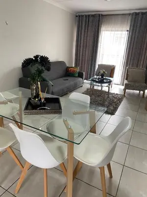 a living room with a glass table and white chairs at IRIS at THE BLYDE in Pretoria