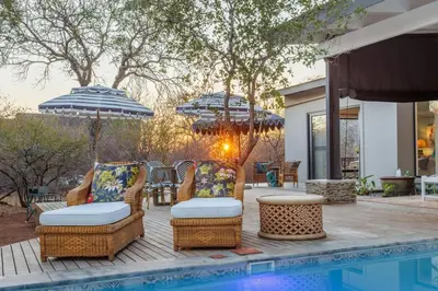 a patio with chairs and umbrellas next to a pool at Bushveld Villa w Pool, Firepit & Outdoor Living in Hoedspruit