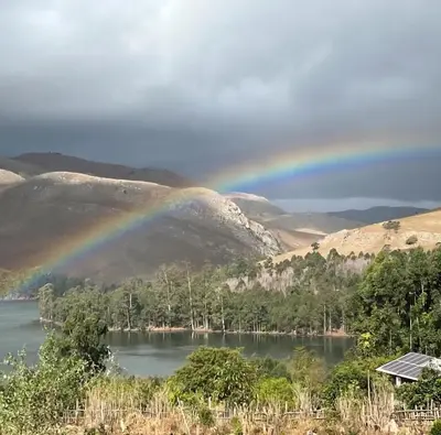 a rainbow over a lake with trees and mountains at Bushbaby Cabin in Louwʼs Creek