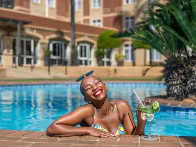 a girl in a bikini holding a drink next to a pool at ANEW Hotel Centurion Pretoria in Centurion