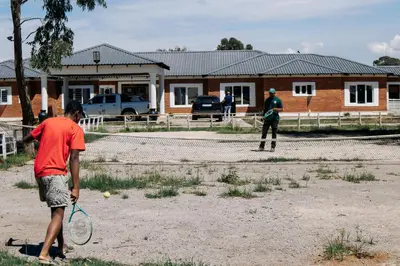 two men playing tennis on a dirt court at La Grande in Benoni