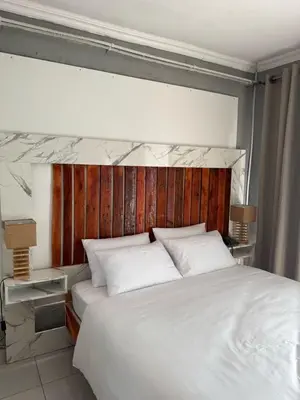 a bedroom with a white bed with a wooden headboard at Amai Guesthouse in Thohoyandou