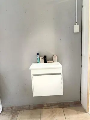 a white shelf against a gray wall with a bottle on it at La Bushka Guesthouse in Bela-Bela