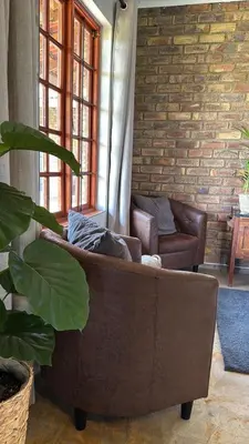 a brown couch in a living room with a brick wall at EquiRest Horse & Human Country Stay in Midrand