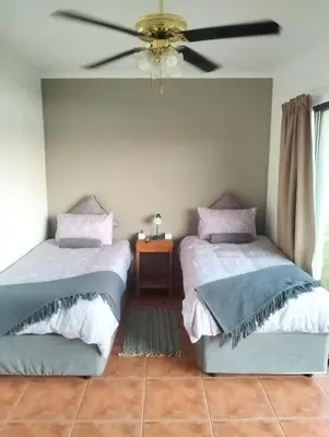 two beds in a room with a ceiling fan at Witbank Dam Self Check In in Witbank