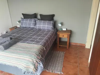 a bedroom with a bed with a gray blanket and a table at Witbank Dam Self Check In in Witbank