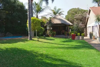 a house with a grass yard with a thatch roof at Khayamanzi Guesthouse in Hartbeespoort