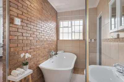 a bathroom with a white tub and a brick wall at Lodge At The Link in Kempton Park