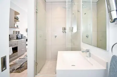 a white bathroom with a shower and a sink at Stylish Penthouse Studio in Ellipse Waterfall in Midrand